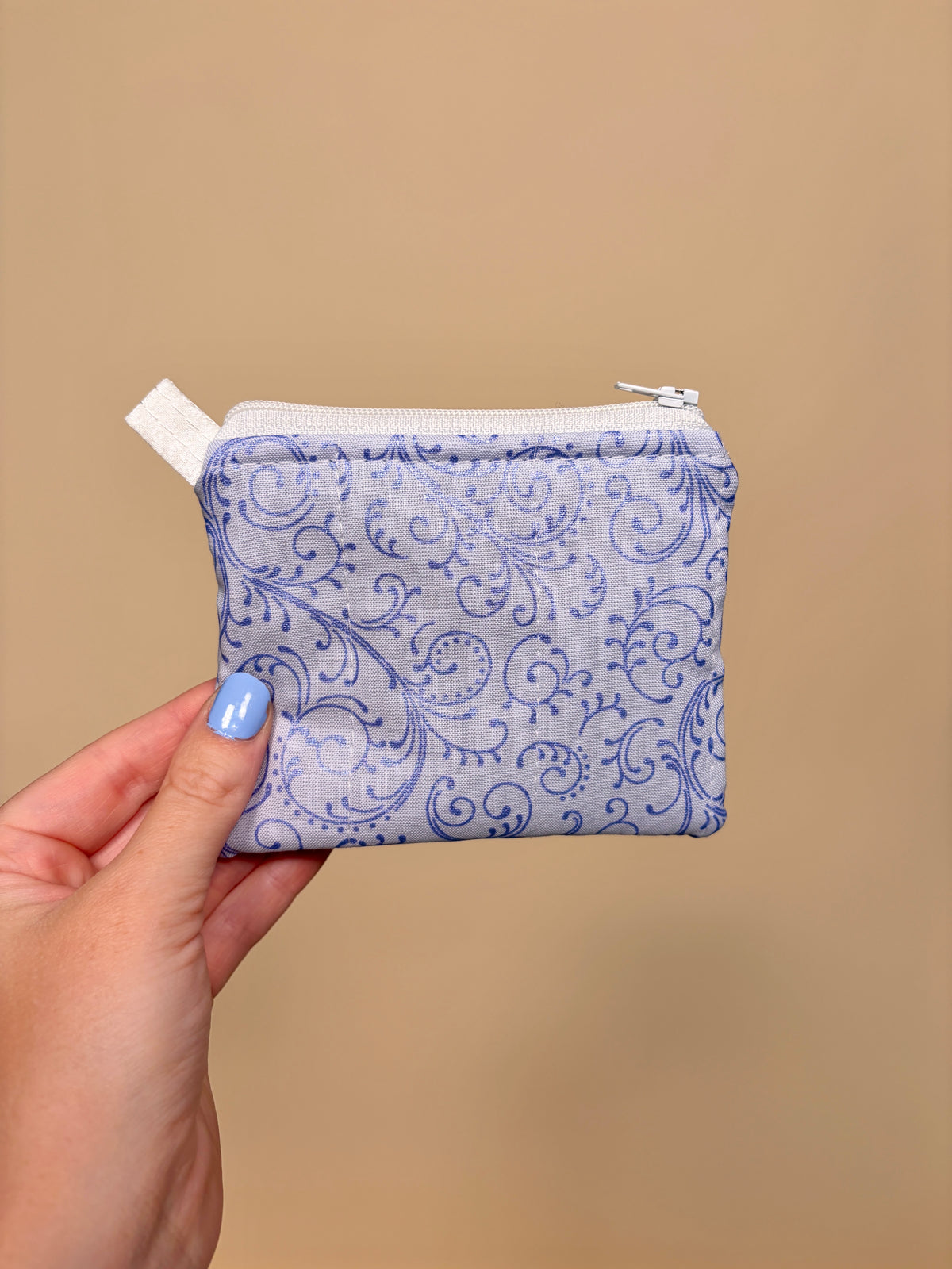 Hand holding a small pouch with blue floral pattern against a beige background