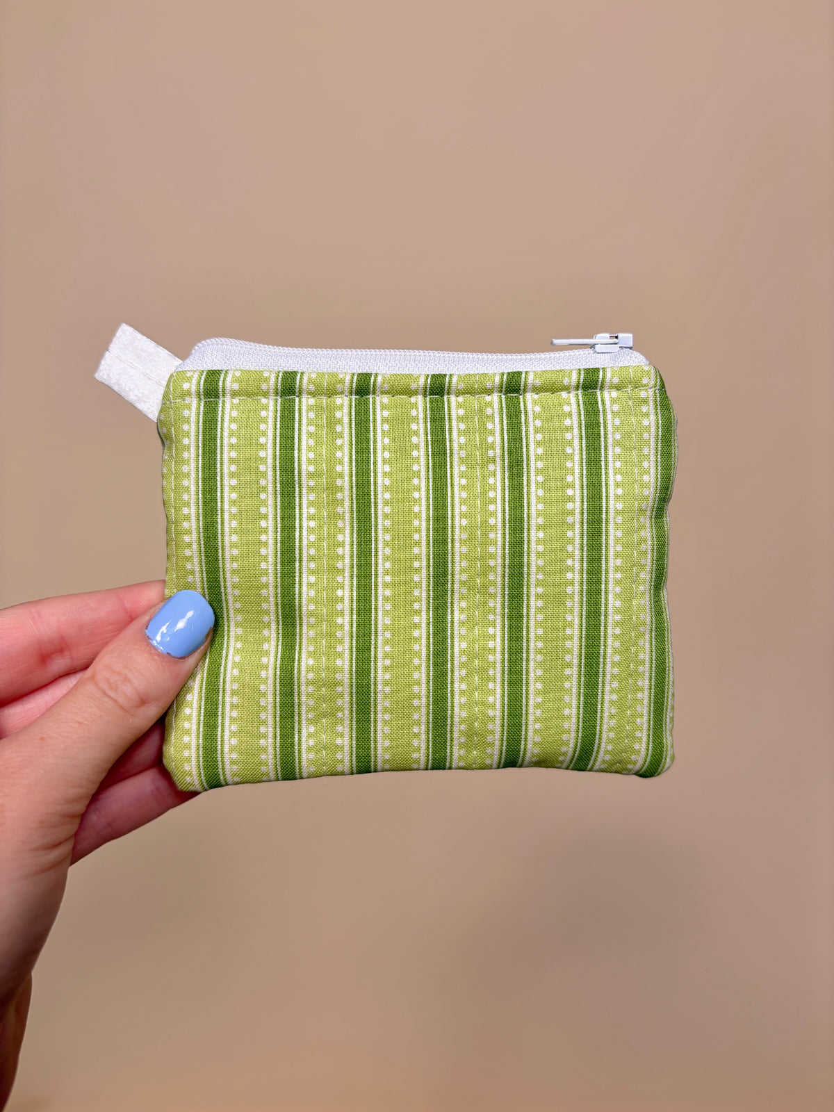 Hand holding a green striped fabric pouch against a beige background