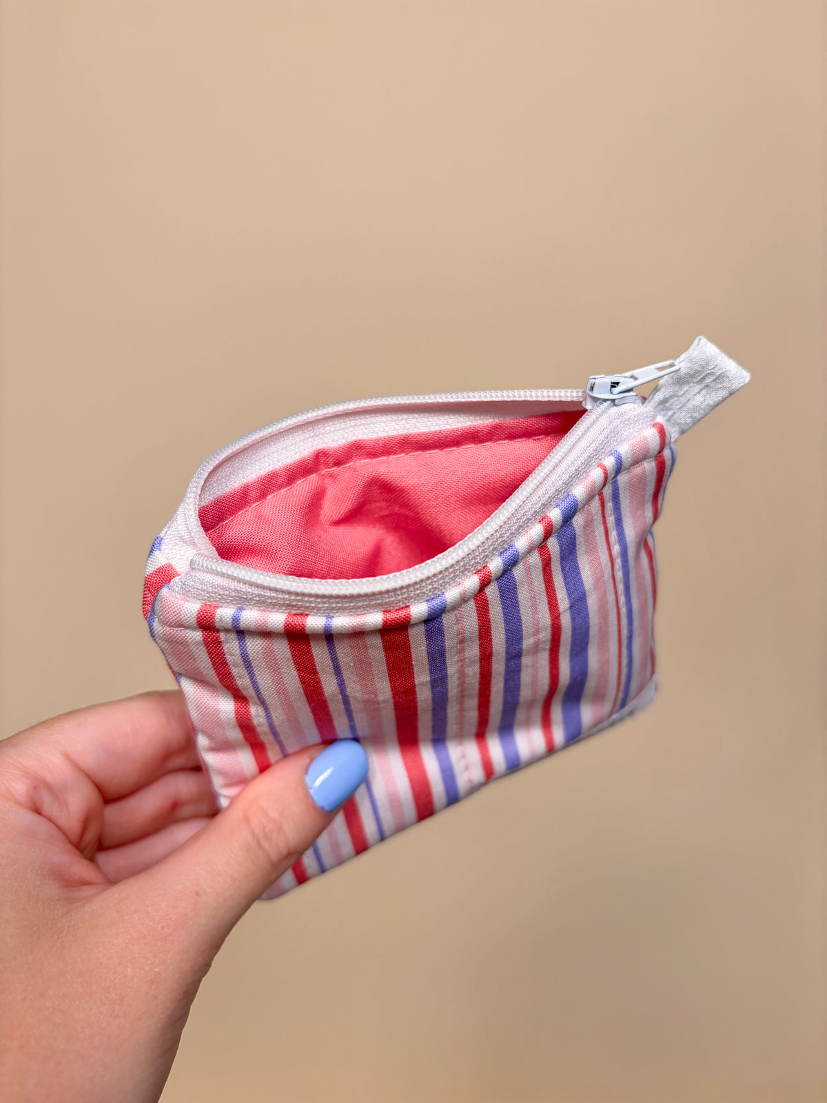 Hand holding a small striped pouch with a pink interior against a beige background