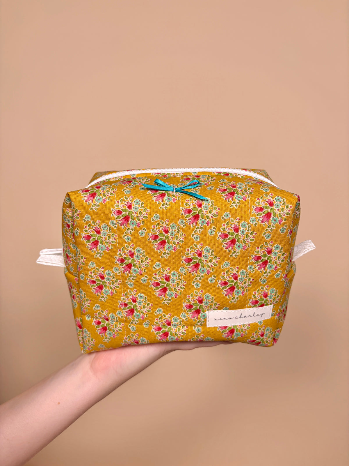 Floral bow makeup bag in mustard yellow with zip top and brand patch