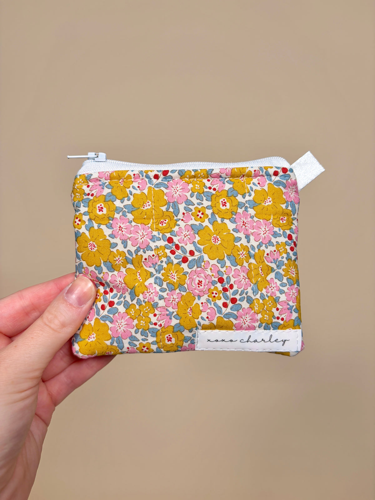 Floral patterned pouch held by a hand against a beige background