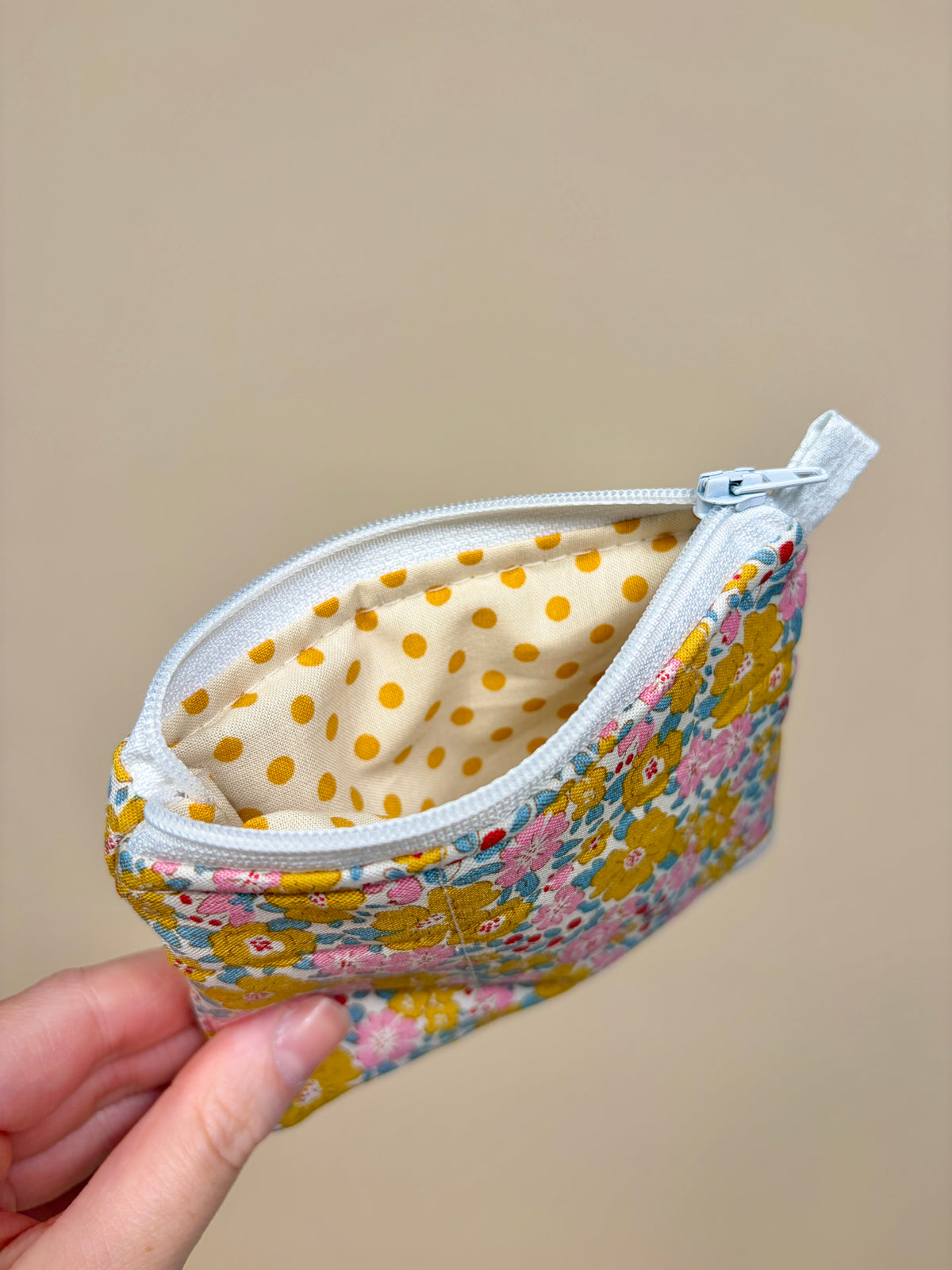 Floral fabric pouch with a white zipper held by a hand against a beige background