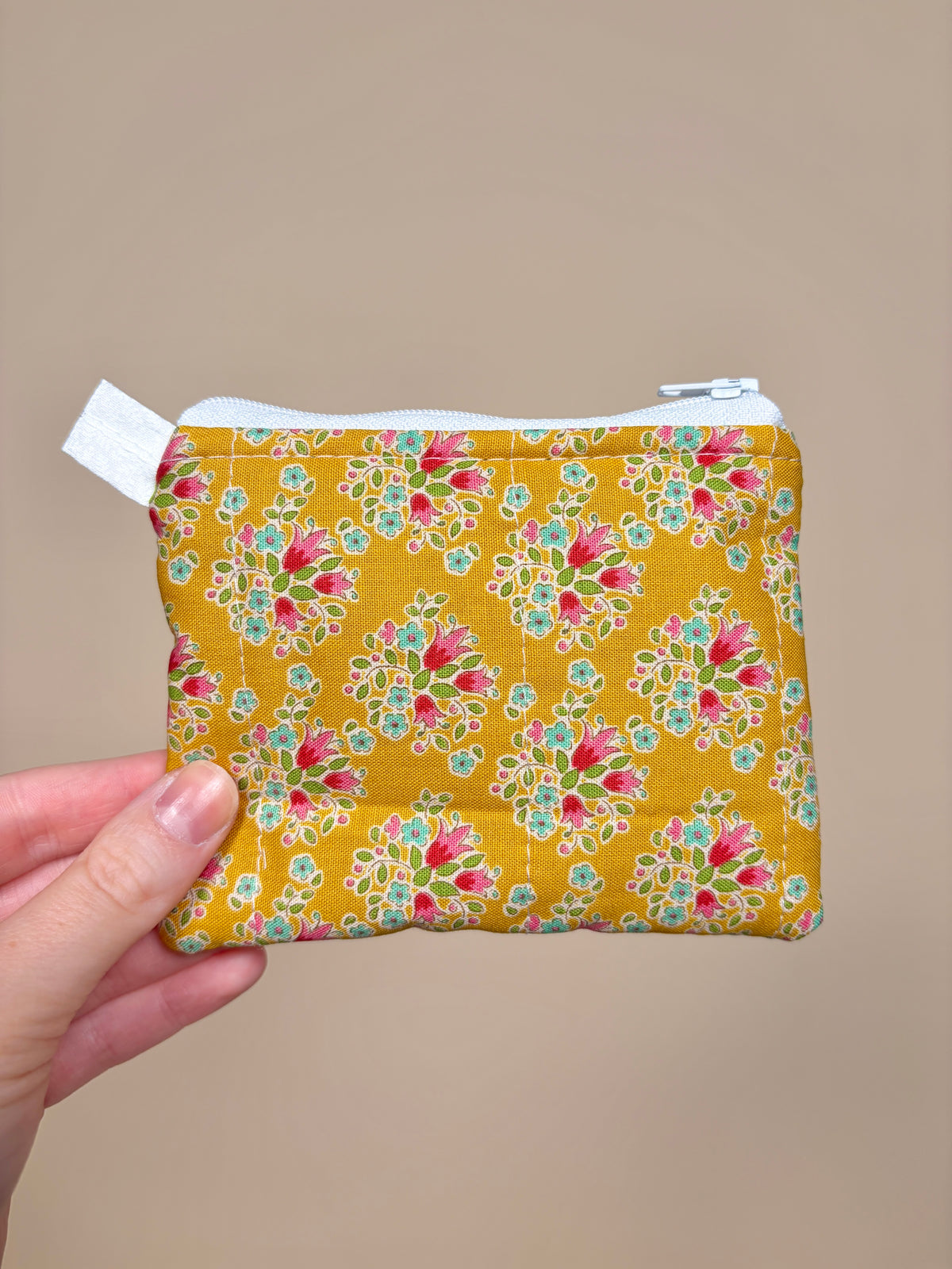 Hand holding a yellow floral-patterned pouch against a beige background
