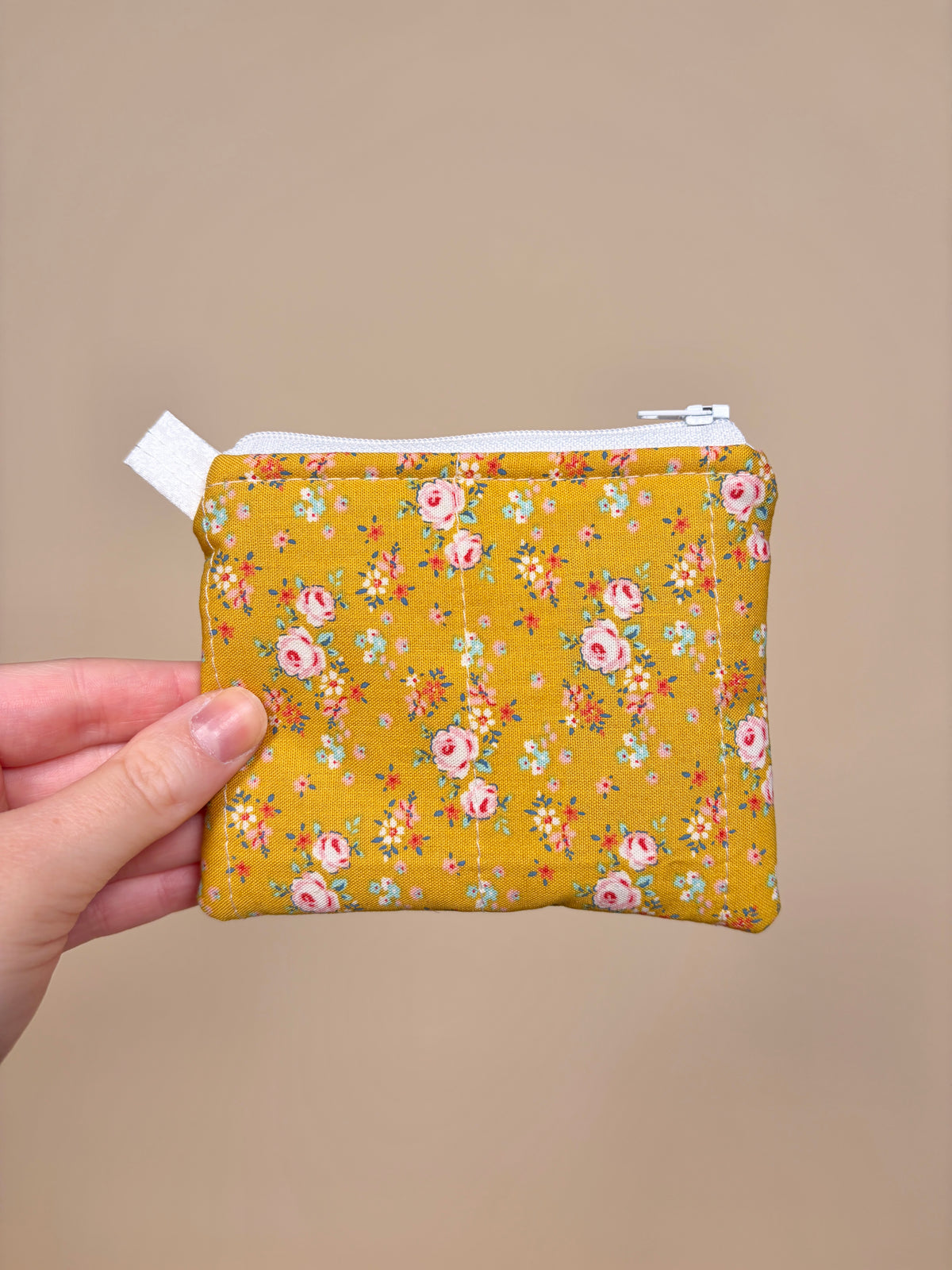 Hand holding a yellow floral-patterned pouch against a beige background