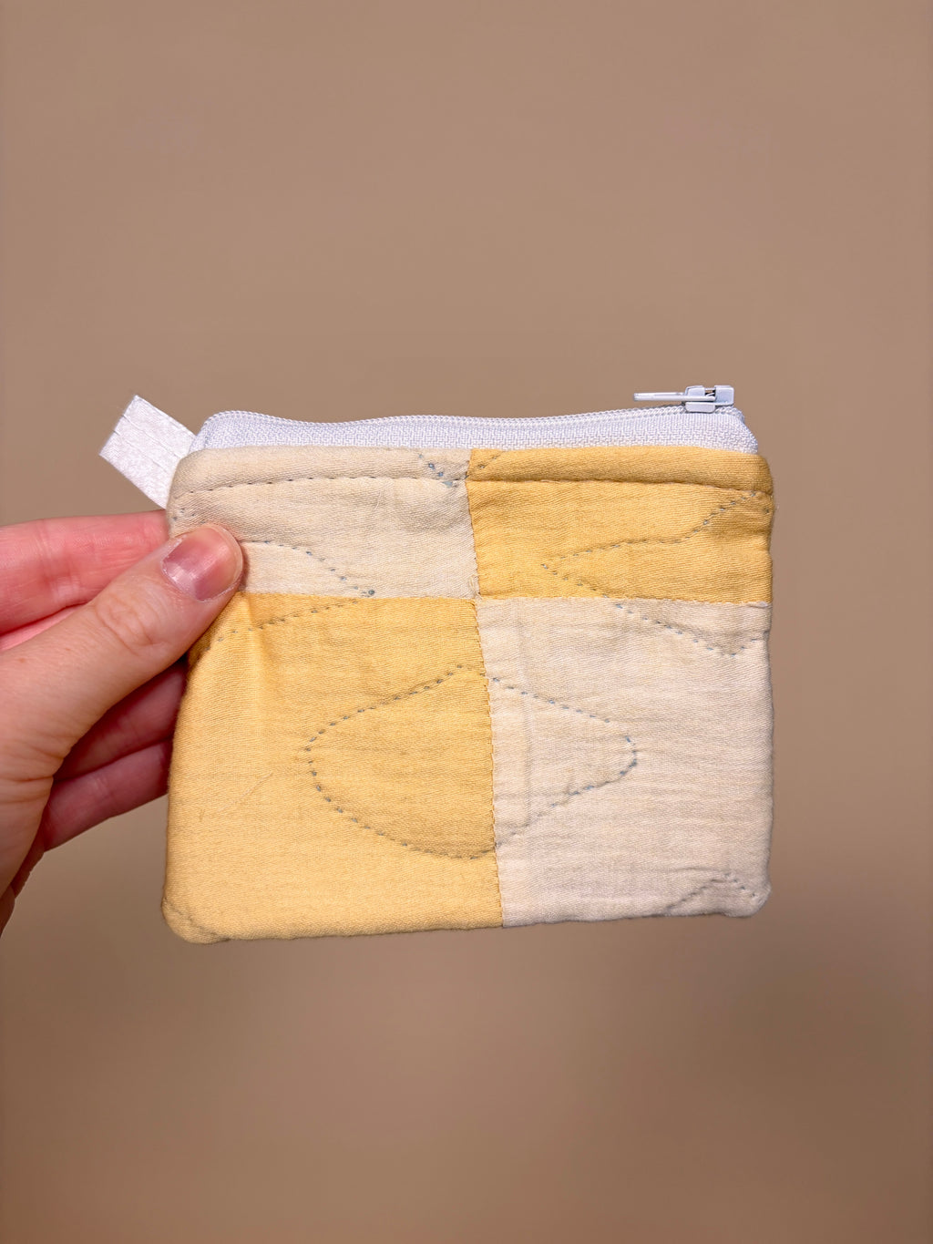 Hand holding a small quilted pouch with yellow and beige pattern against a brown background