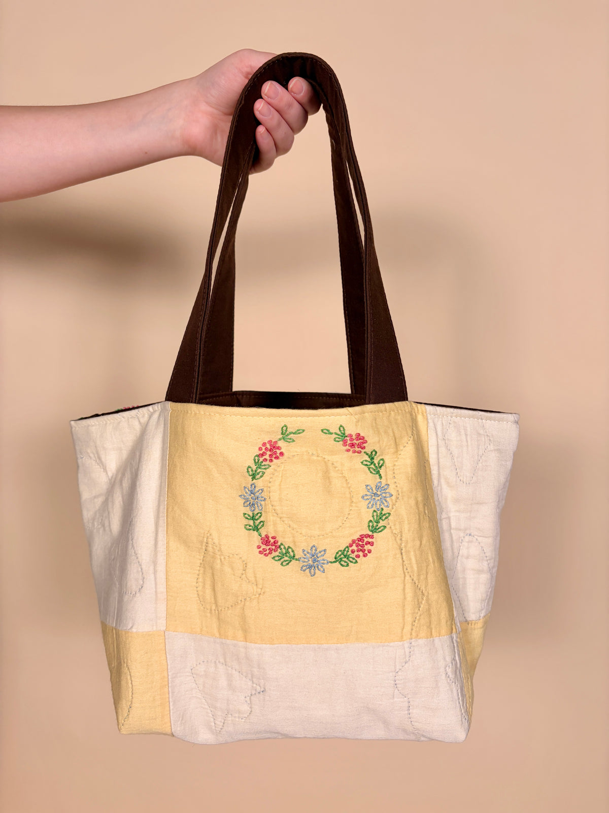 Mini patchwork tote bag with centered wreath print, white and yellow panels, brown handles