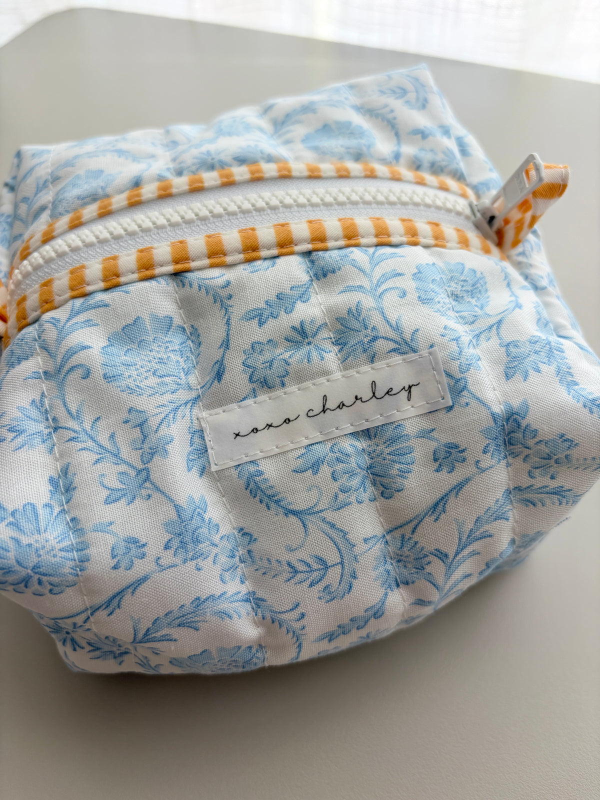 Blue floral zip bag with front label pocket and orange striped trim