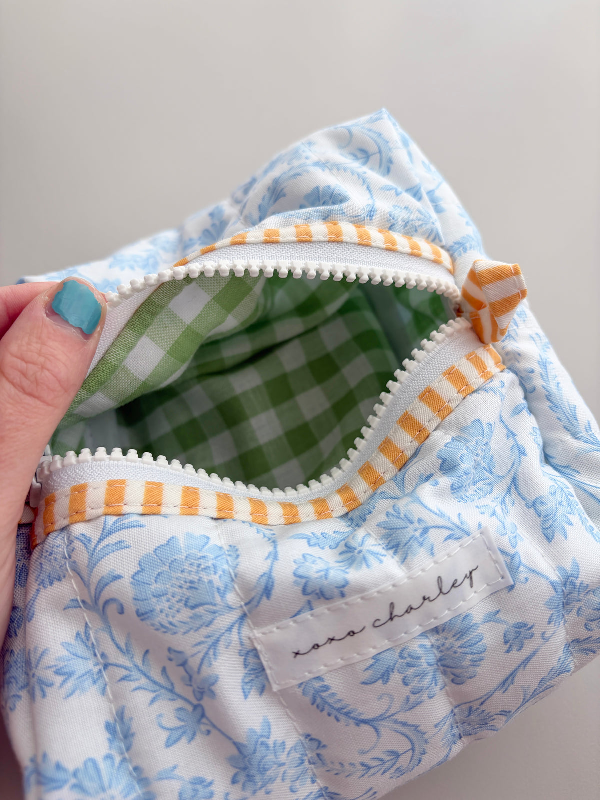Blue floral zip bag opened to green gingham lining with white zipper trim