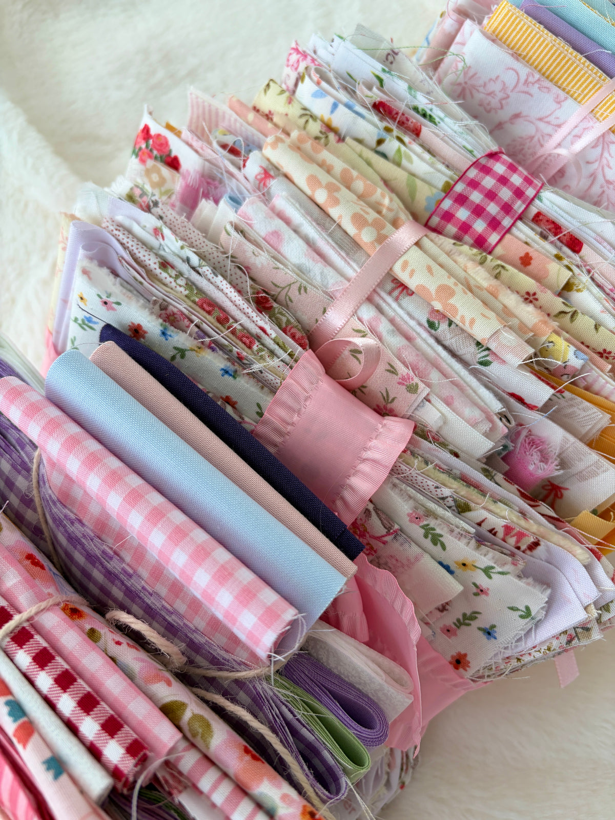 Pastel fabric rolls and folded squares with gingham and floral prints, ribbon bundle
