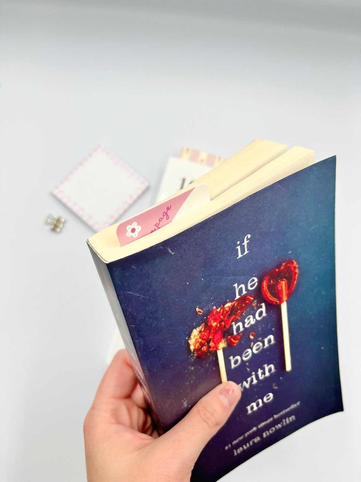 Blue book bookmark held in hand, with red heart graphic and pink floral trim
