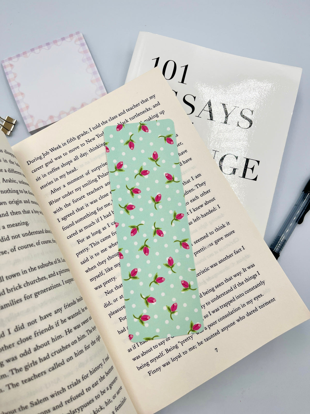 Teal rose-pattern bookmark on open book, full view of pink blossoms
