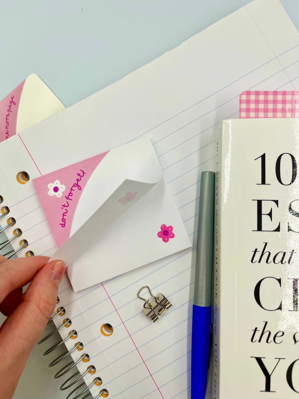 Hand holding white sticky note with pink border and flower icon on notebook