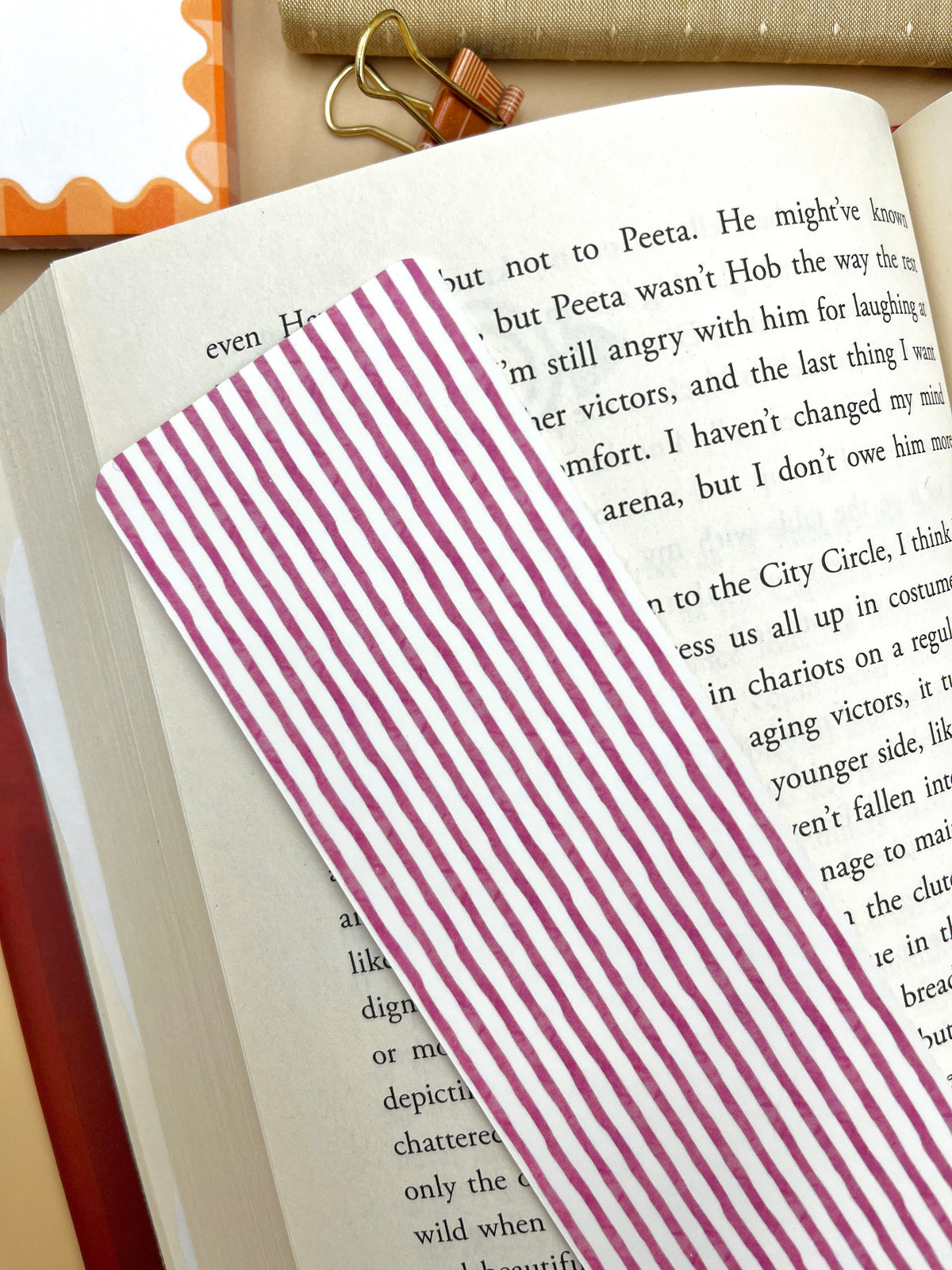 Plum striped bookmark with vertical magenta-and-white stripes, tucked in book text.