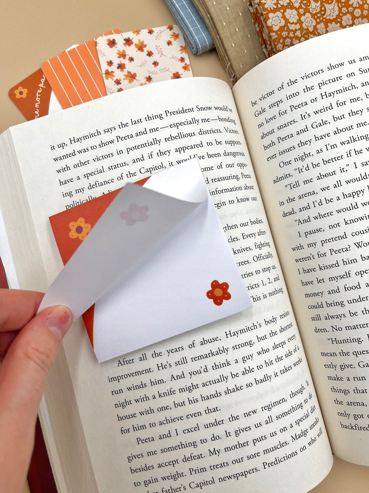 Hand holding an orange floral sticky note tab on open book pages