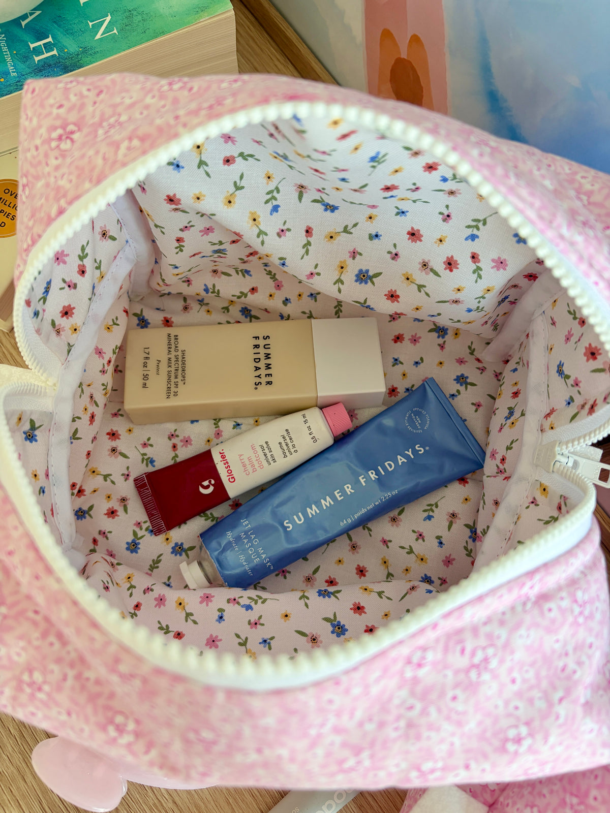 Mini pink floral makeup pouch, open showing assorted skincare tubes and boxes inside