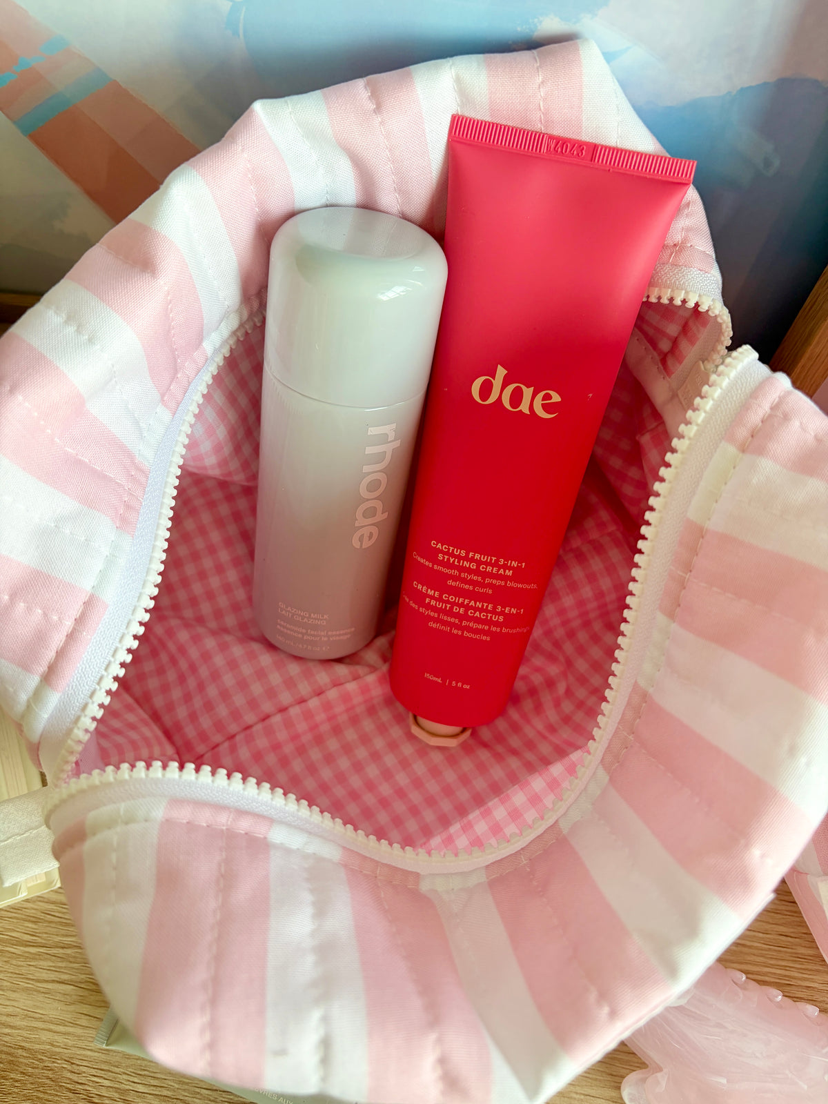 Pink and white striped makeup bag with zipper, holding skincare bottles and tube