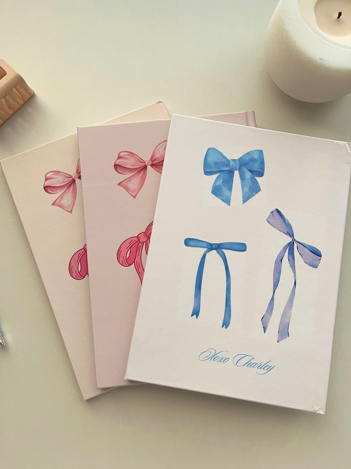 Three reading journals with pink and blue bow illustrations stacked on a desk.