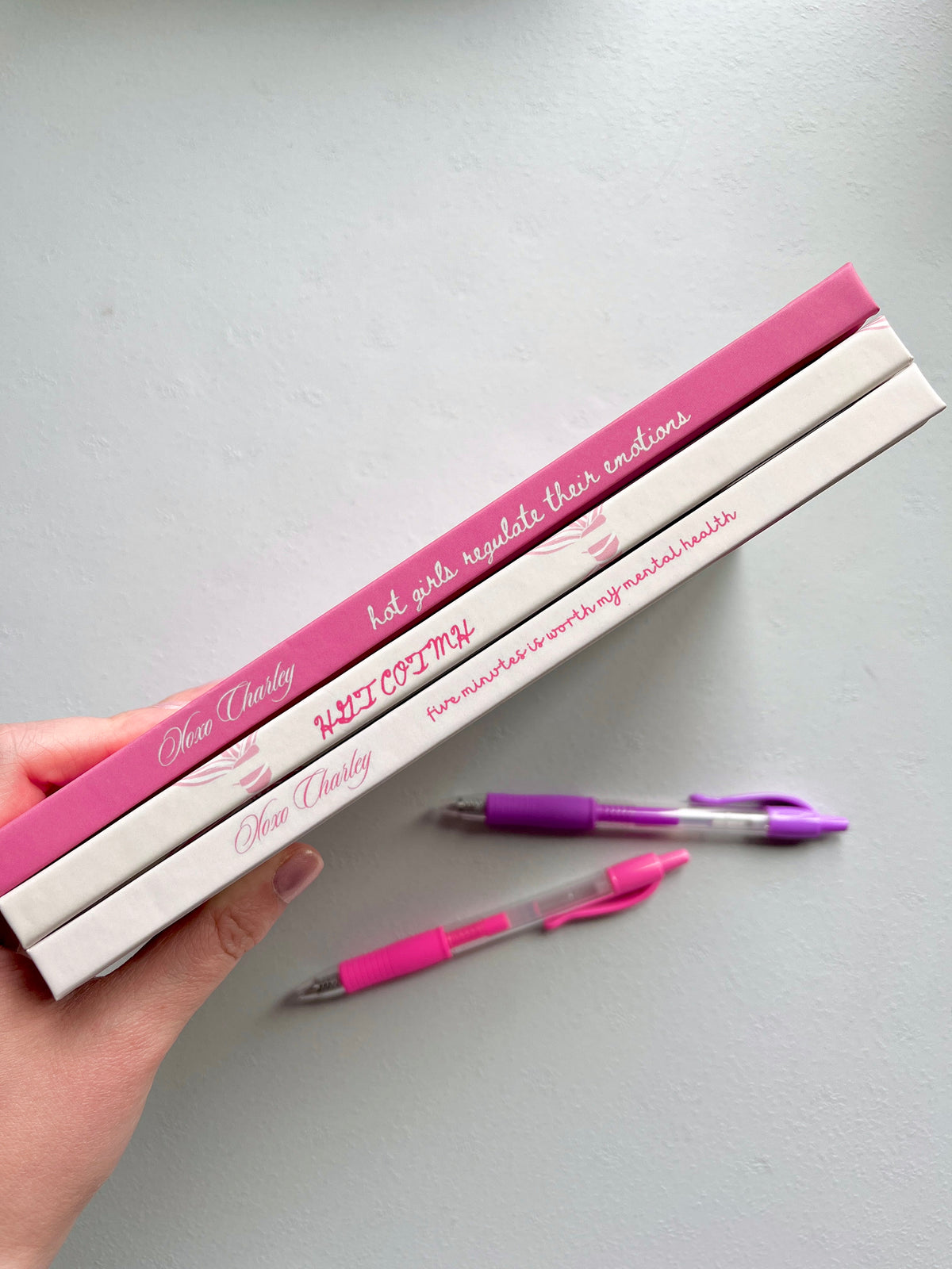 Mental health journal set, hands holding closed notebooks with pink pens